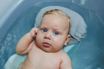 A 4-month-old little boy bathes in a bathtub while lying on a stand. Caring for a newborn baby, bathing the baby