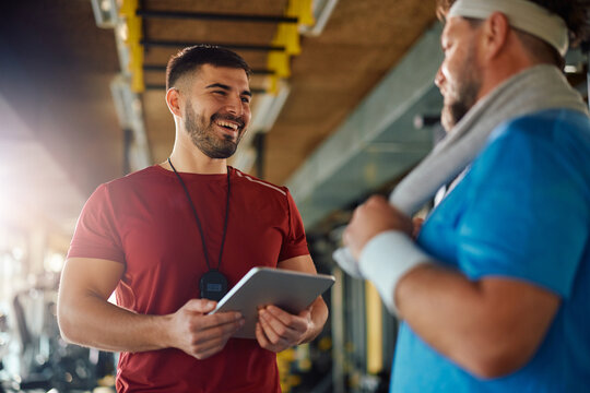 Happy personal trainer talking to his mature client during exercise class in gym.