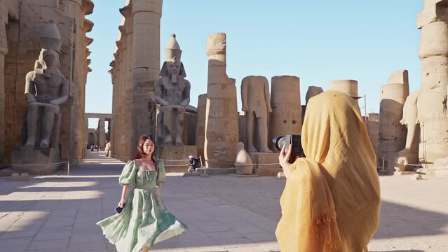 beautiful tourist holding a camera taking pictures of ramsses statue and her family in luxor temple, Luxor, Egypt.