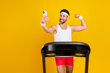 Photo of cheerful strong guy sportswear running treadmill showing biceps tacking selfie device...