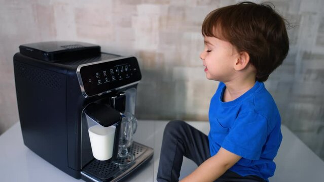 Cute lovely Caucasian boy sits near the coffee machine. Little kid waiting for cappuccino cup.