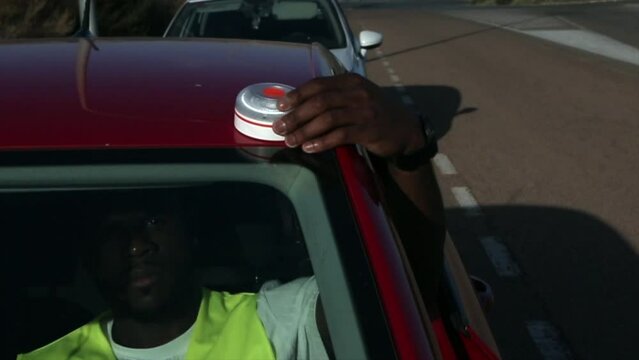 African-American man placing the new emergency light for broken-down vehicles (V16 light beacon), which is to be replaced by triangles. road safety.