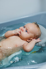 A 4-month-old little boy bathes in a bathtub while lying on a stand. Caring for a newborn baby, bathing the baby