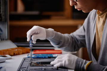 Close-up of repairman fixing broken smartphone with screwdriver sitting at table in workshop
