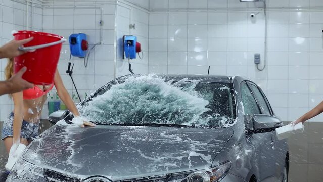  Two sexy girls (MR) clean car by sponges during water splash from bucket in car-wash box (PR). Slow motion