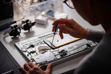 Unrecognizable male technician repairing computer using screwdriver in modern workshop