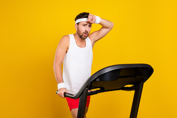 Portrait of exhausted person wipe sweat forehead intense run treadmill isolated on yellow color...