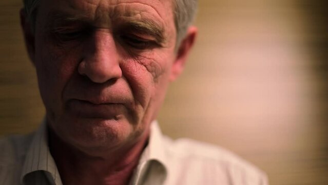 Wrinkled face of serious elderly man which looks downward. Slow motion