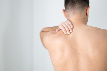 Rear view of a shirtless young man holding his neck in pain isolated on white background, man giving himself a massage on his neck, shirtless man touching his neck, stress, neck pain, upper back pain