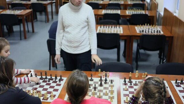 six people play chess against one man in room with many chessboards on tables