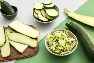 Wooden board and bowls with slices of fresh green zucchini on colorful background