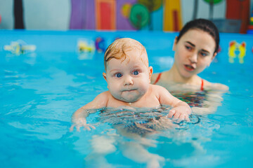 Training of a newborn baby in the pool with a swimming coach. A pool for babies. Child development. A small child learns to swim in the pool