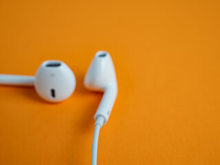 White headphones with cable on an orange background. Headphones close-up.