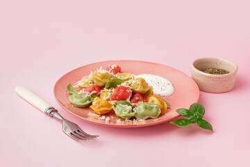 Plate of boiled colorful dumplings with cheese, basil and sour cream on pink background