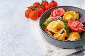 Bowl of boiled colorful dumplings with spinach and tomatoes on white background