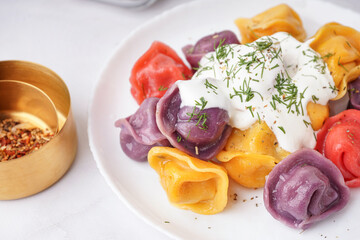 Plate of boiled colorful dumplings with sour cream and dill on white background