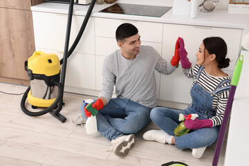 Happy young couple with cleaning supplies giving each other high-five in kitchen