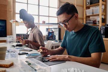 Fototapeta premium Professional caucasian repairman soldering motherboard, his black colleague working on background