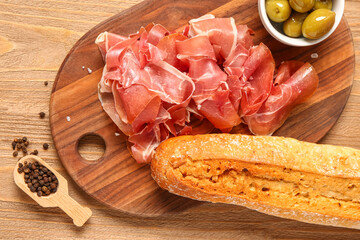 Board with slices of tasty prosciutto and bread on wooden background