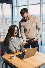 Fototapeta premium Working day in a modern office with workers in casual clothes, male and female colleagues working with a laptop on a modern project.