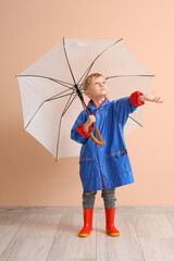 Little boy in rubber boots with umbrella near beige wall