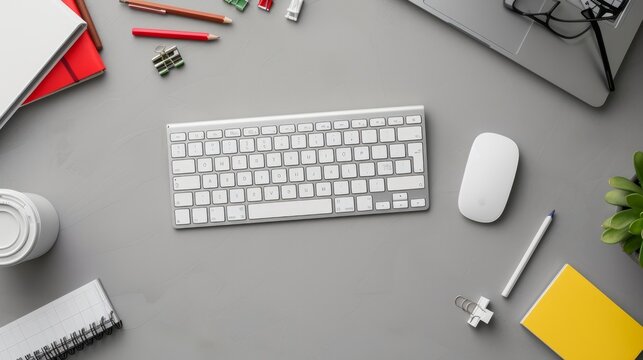 modern Mac computer keyboard and mouse set diagonally on a grey desk, surrounded by assorted office supplies