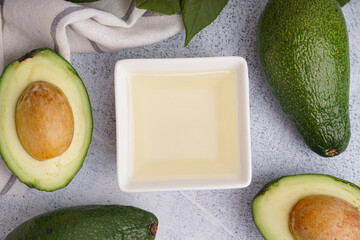 Fresh avocados and bowl with essential oil on white grunge background