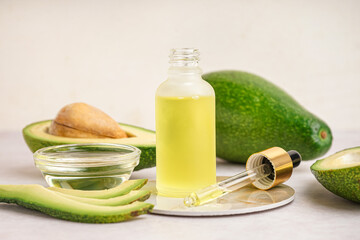 Fresh avocados with glass bowl and bottle of essential oil on beige background