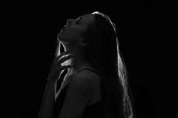 Silhouette of young woman touching her neck on black background, closeup