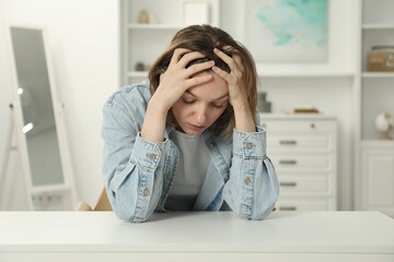 Sad young woman sitting at white table in room