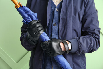 Man in stylish leather gloves holding umbrella against color wall, closeup