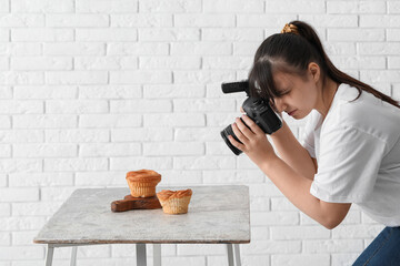 Female food photographer taking picture of cakes near white brick wall