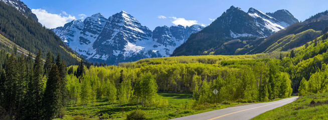 Maroon Bells - A panoramic view of Maroon Bells rising high in lush green Maroon Creek Valley, as seen from side of Maroon Creek Road, on a sunny Spring evening. Aspen, Colorado, USA.