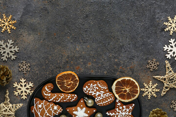 Plate of Christmas gingerbread cookies with dried orange slices and decorations on dark background