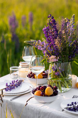 Beautiful romantic outdoor wedding decor in a field. Table decorated with purple lupines flowers. Wineglasses with white wine. Sunset, summer, golden hour. Perfect surprise date for loving couple
