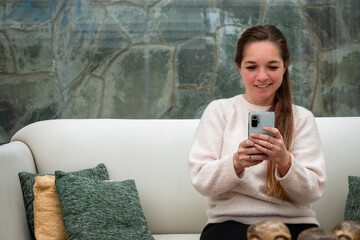 Mujer interactuando con su teléfono móvil sentada en su sofá
