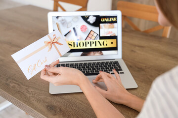 Young woman with gift card and laptop shopping online in kitchen, closeup
