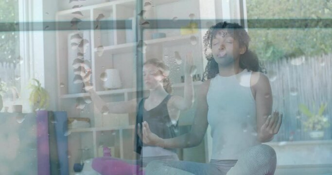 Animation of water droplets on window over happy diverse teenage girls practicing yoga meditation