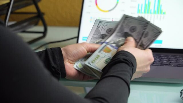 4K close up footage of female hands counting 100 dollar banknotes in front of laptop screen with diagrams.