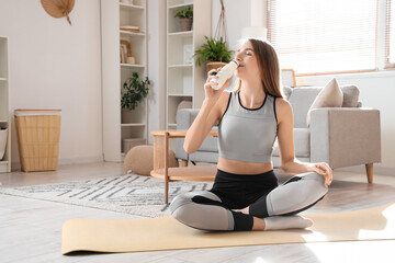 Sporty young woman drinking tasty yoghurt at home