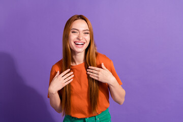 Portrait of young smiling girl in orange t shirt touching chest when someone saying compliments for...