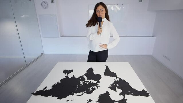 Woman with microphone arrange world map puzzle on table in room
