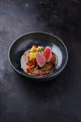 Traditional fried venison back filet with kaki fruit, carrots and potato puree in game sauce served as close-up on Nordic design plate