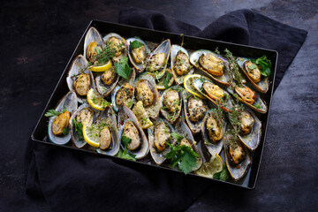 Traditional New Zealand green scallops halved and gratinated with herbs, spices and garlic served in white wine as a close-up on a rustic baking tray