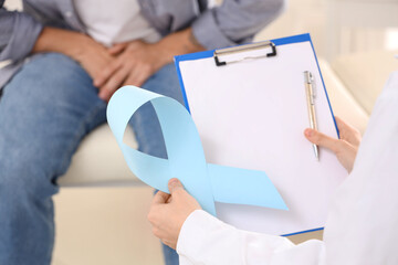 Urologist with blue ribbon and clipboard at hospital, closeup. Prostate cancer awareness concept
