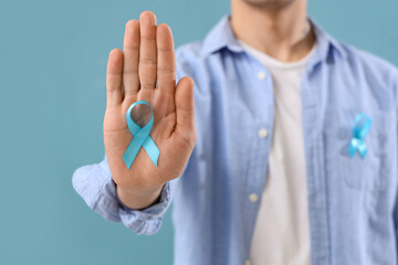 Young man with blue ribbon on color background, closeup. Prostate cancer awareness concept