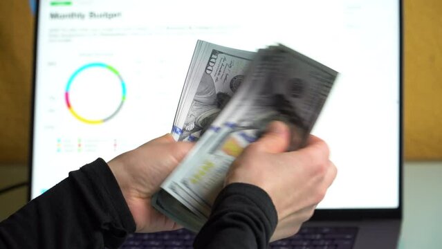 4K close up footage of female hands counting 100 dollar banknotes in front of laptop screen with diagrams.