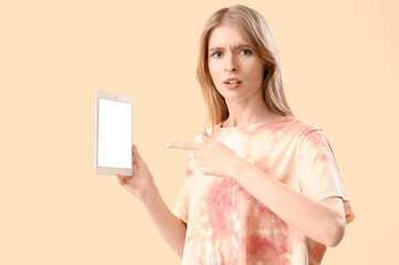 Young woman pointing at tablet computer on beige background. Accusation concept