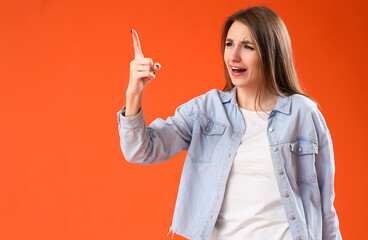 Young woman pointing at something on orange background. Accusation concept