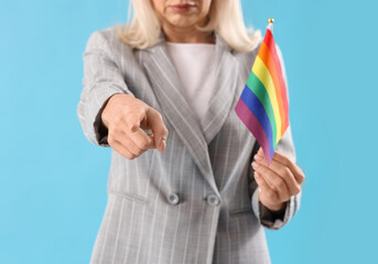 Mature woman with LGBT flag pointing at viewer on blue background, closeup. Accusation concept